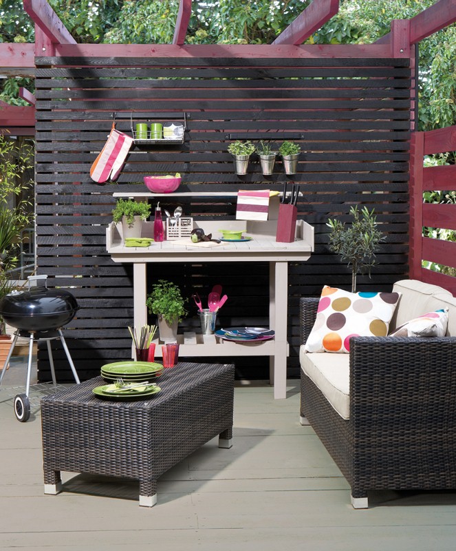 An outdoor seating area underneath a pergola, with an array of wicker garden seating and a barbeque